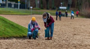 Zwei Personen sammeln Müll an Sandstrand.